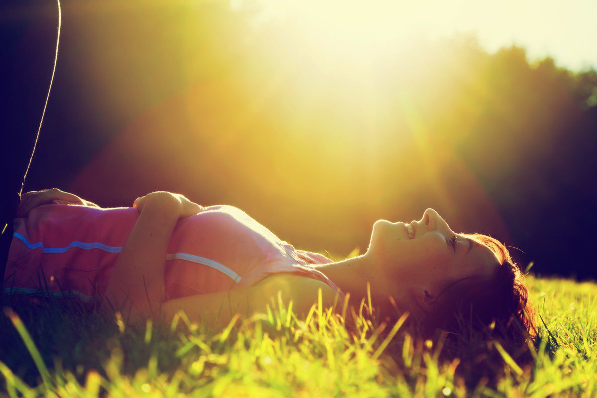 Woman laying in grass with sun shining.