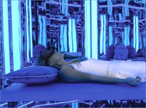 Woman laying on bed in blue light room.