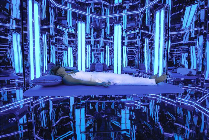 Woman lying in a mirrored room with blue light.